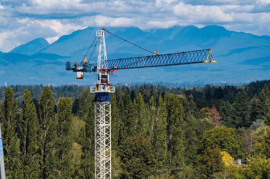 Completed tower crane rising above the trees at Clayton Crest in West Clayton, Surrey, with the North Shore mountains behind it