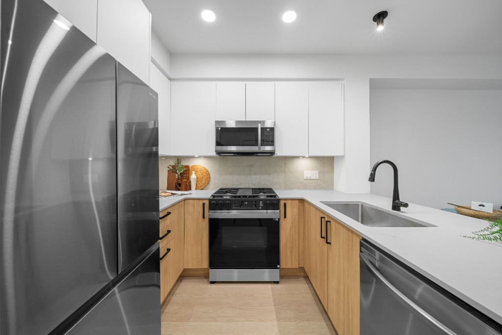 Kitchen at The Commons condos in Willoughby, Langley, with wood cabinets, quartz counters and a gas range