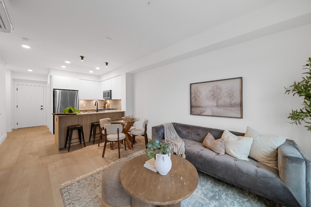 Open-concept living room and dining area at The Commons condos in Willoughby, Langley, with a grey sofa and kitchen island